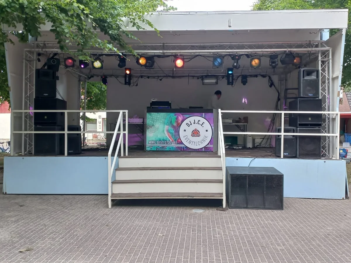 Aufgebaute Eventbühne mit Lichtanlage, Boxen und DJ-Pult im Freien