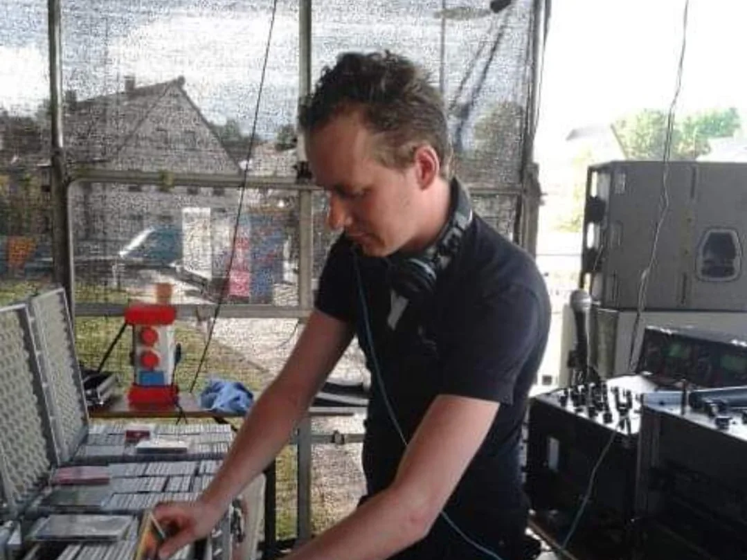 DJ J.C.E. am Pult, greift zu einer CD aus dem offenen Plattenkoffer
