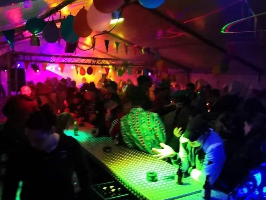 Gut gefülltes Partyzelt mit Luftballons und beleuchteter Bar