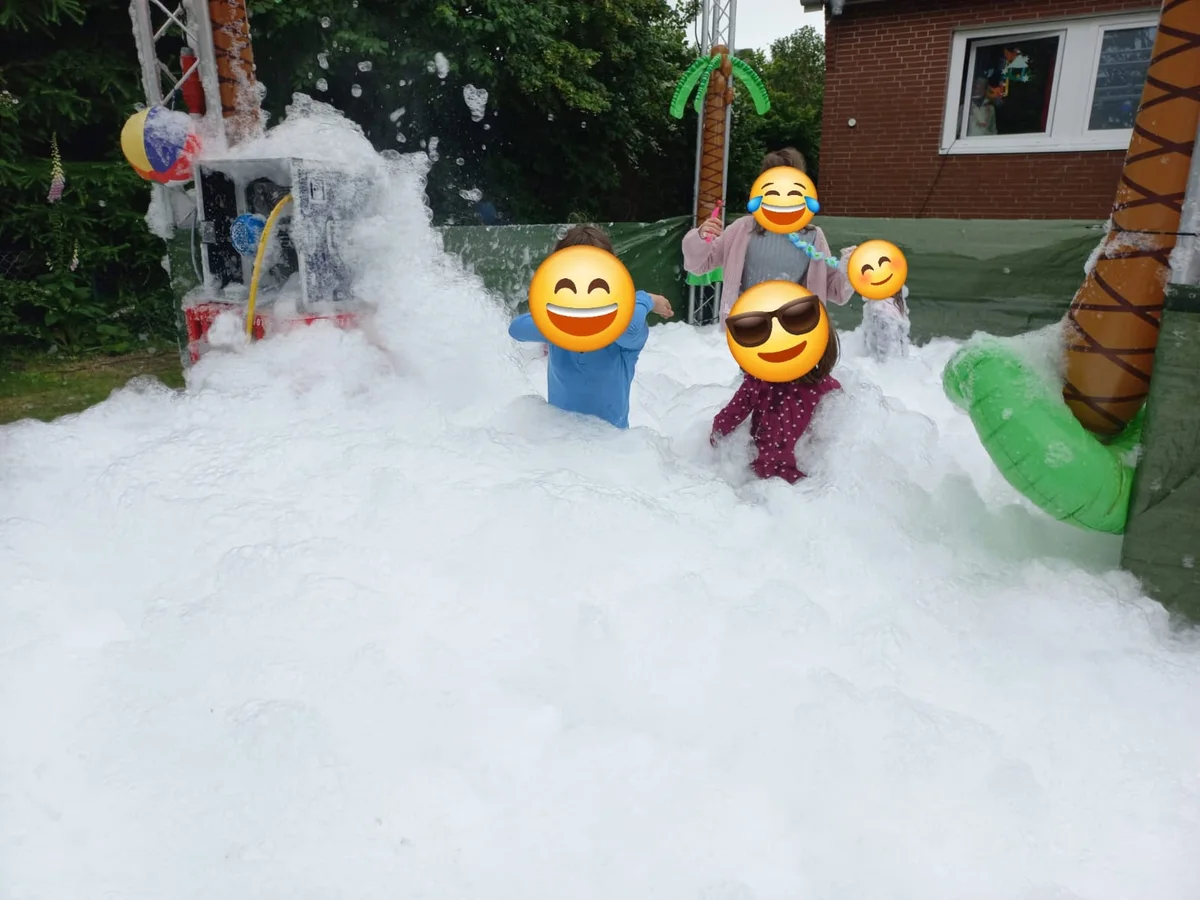 Kinder spielen im Schaum der Schaumkanone in einem Garten